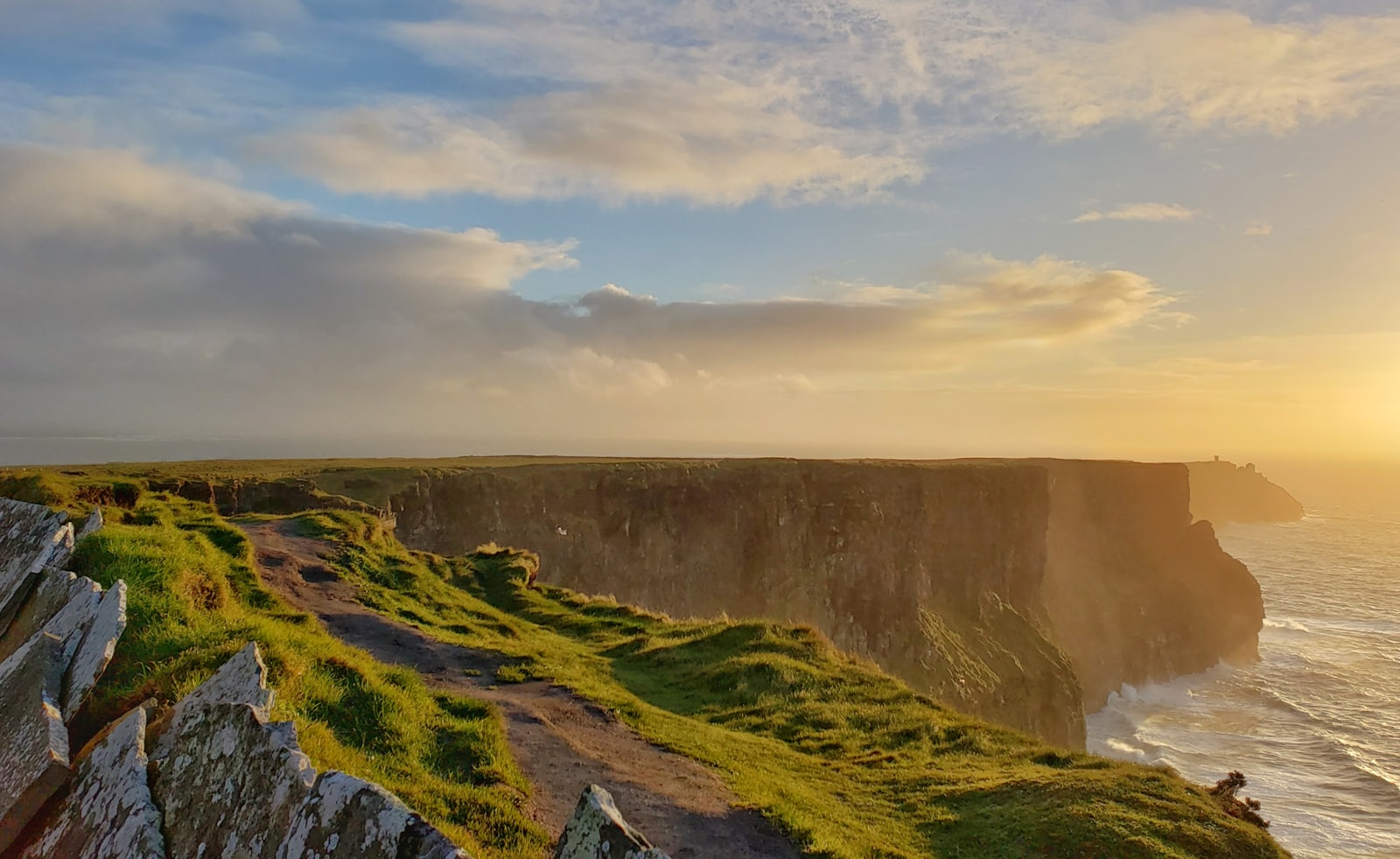A coastal cliff path overlooking the sea in golden evening light